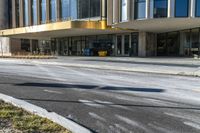 street sign sitting next to grass and sidewalk in front of building with windows and parking lot behind it