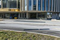 street sign sitting next to grass and sidewalk in front of building with windows and parking lot behind it