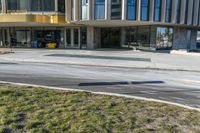 street sign sitting next to grass and sidewalk in front of building with windows and parking lot behind it