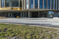 street sign sitting next to grass and sidewalk in front of building with windows and parking lot behind it