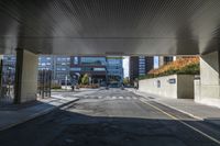 the empty street with high - rise buildings is under an overpassed bridge at the entrance