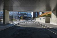 the empty street with high - rise buildings is under an overpassed bridge at the entrance