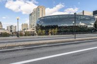 an open area next to a big building with large windows next to a street with some cars parked on it