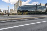 an open area next to a big building with large windows next to a street with some cars parked on it