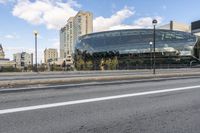 an open area next to a big building with large windows next to a street with some cars parked on it