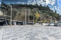 a square stone patio with a building in the background with the sky reflected in the building