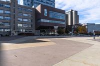 two buildings with a person skateboarding across the sidewalk from one another while another sits on a bicycle in the background