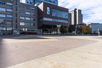 two buildings with a person skateboarding across the sidewalk from one another while another sits on a bicycle in the background