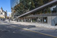 an empty street in front of a modern building with large windows with glass at the top of each building