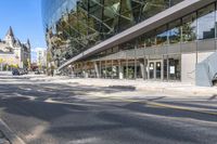 an empty street in front of a modern building with large windows with glass at the top of each building