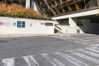 an empty street with concrete walls in front of a glass building that has signs and other things attached to it