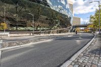 several pedestrians are walking on an empty street near the modern building and sky scrapes