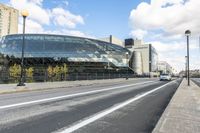 a road with some cars on it next to some buildings and a blue sky with clouds