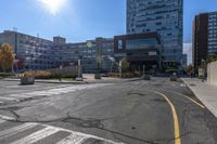 a large empty intersection with buildings in the background on a sunny day with sunshine flares