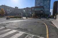 a large empty intersection with buildings in the background on a sunny day with sunshine flares