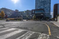 a large empty intersection with buildings in the background on a sunny day with sunshine flares