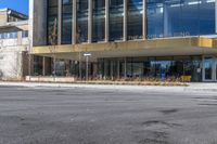 a building with many windows on a street corner in front of a sidewalk with bushes