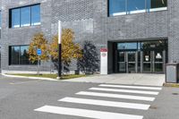 a white cross walk on a small city street with a building behind it, a car is parked in the driveway with no doors