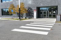 a white cross walk on a small city street with a building behind it, a car is parked in the driveway with no doors