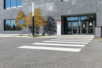 a white cross walk on a small city street with a building behind it, a car is parked in the driveway with no doors