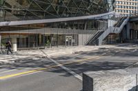 the empty road under a bridge leads into an office building next to an entrance and stairs