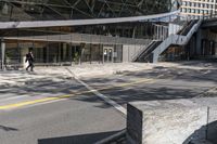 the empty road under a bridge leads into an office building next to an entrance and stairs