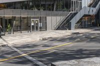 the empty road under a bridge leads into an office building next to an entrance and stairs