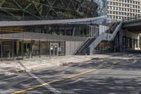 the empty road under a bridge leads into an office building next to an entrance and stairs