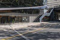 the empty road under a bridge leads into an office building next to an entrance and stairs