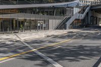 the empty road under a bridge leads into an office building next to an entrance and stairs