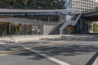 the empty road under a bridge leads into an office building next to an entrance and stairs