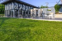 an outside area with several tables and chairs on the grass and a building next to it