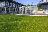 an outside area with several tables and chairs on the grass and a building next to it