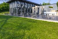 an outside area with several tables and chairs on the grass and a building next to it