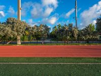 an outdoor sports field in front of a tree and sky with clouds in the background