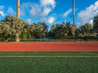 an outdoor sports field in front of a tree and sky with clouds in the background