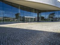 there is an oval building that has a stone pathway in front of it with reflections on the windows