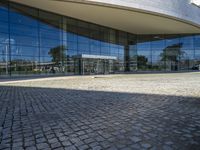 there is an oval building that has a stone pathway in front of it with reflections on the windows