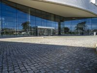 there is an oval building that has a stone pathway in front of it with reflections on the windows