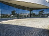 there is an oval building that has a stone pathway in front of it with reflections on the windows