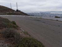 the sky is overcast with a big city in the distance as people walk on the side of a long hill