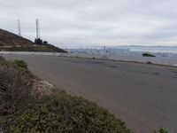 the sky is overcast with a big city in the distance as people walk on the side of a long hill