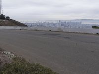 the sky is overcast with a big city in the distance as people walk on the side of a long hill