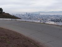 the sky is overcast with a big city in the distance as people walk on the side of a long hill