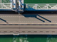 a bridge over the ocean with construction equipment in the background and two people walking on it