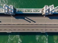 a bridge over the ocean with construction equipment in the background and two people walking on it