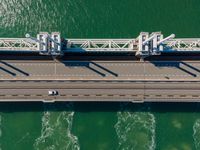 a bridge over the ocean with construction equipment in the background and two people walking on it