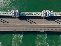 a bridge over the ocean with construction equipment in the background and two people walking on it