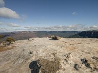 a person sits on top of a rock above a valley, overlooking the horizon in a scenic setting