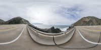 a fish eye lens looking out over a road with rocks on the other side and ocean on the far side